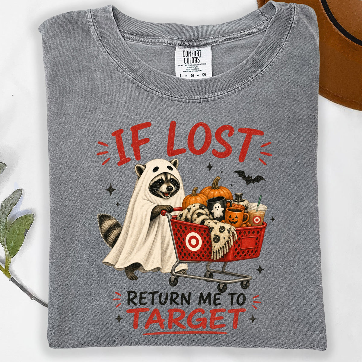 Raccoon in ghost costume pushes shopping cart with pumpkins and text "If Lost Return Me To Target".