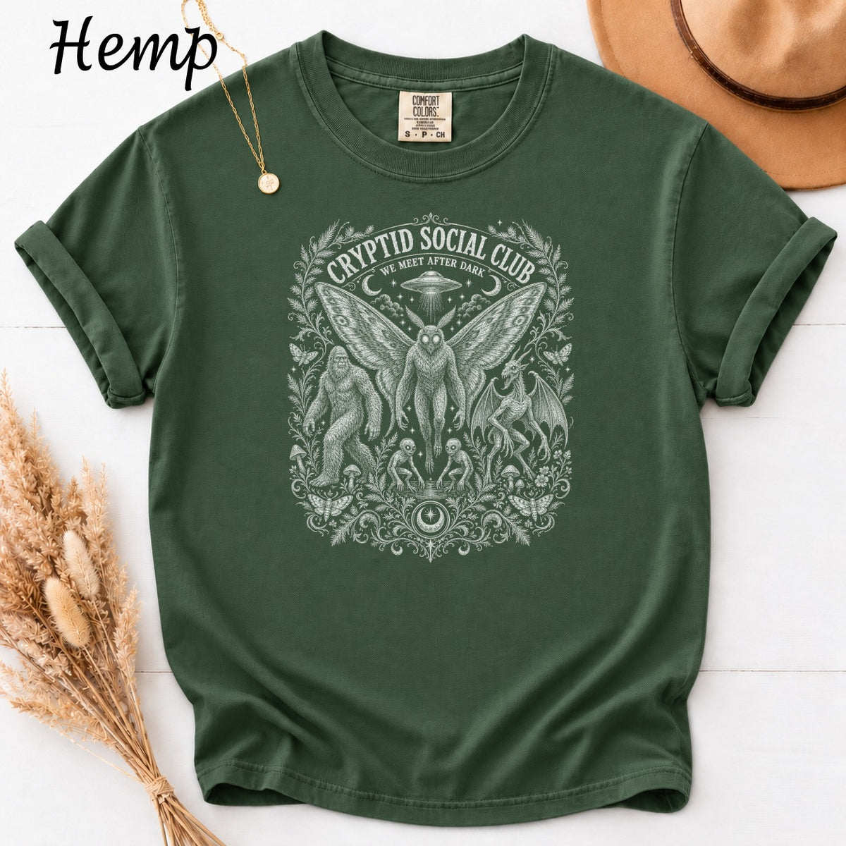 Green t-shirt with white Cryptid Social Club design featuring Mothman, Bigfoot, and dragon.