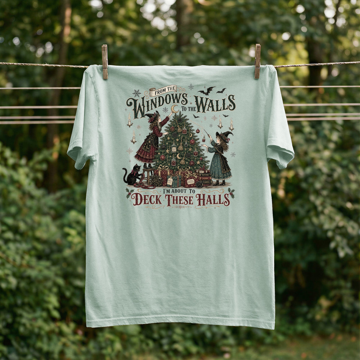 Light blue t-shirt with witches decorating a Christmas tree and the text "I'm About to Deck These Halls".
