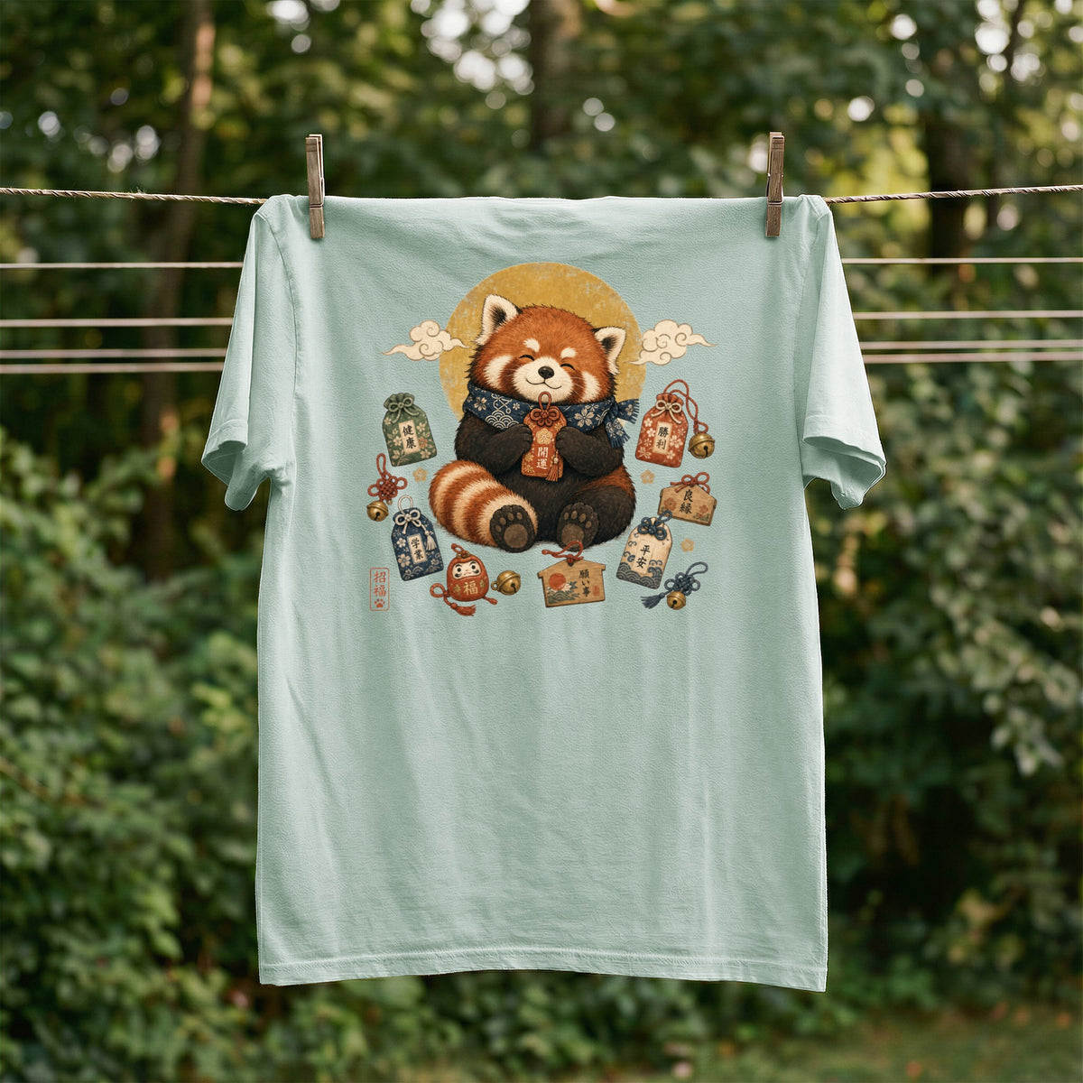 Red panda wearing a scarf sits surrounded by Japanese charms and bells on a light green t-shirt.