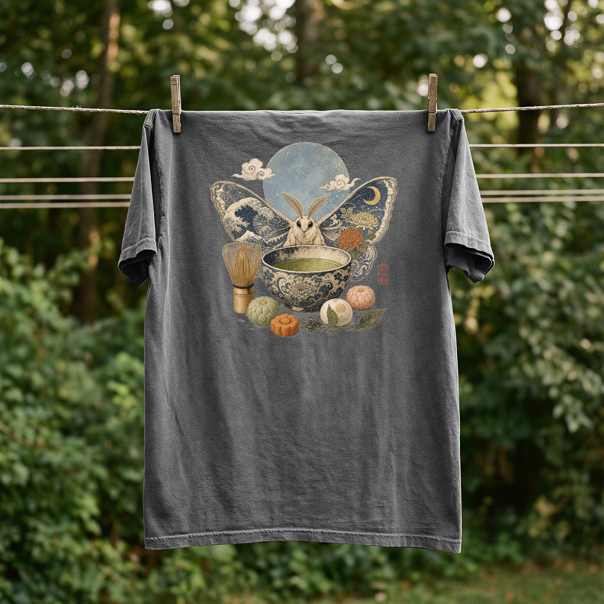 Dark gray t-shirt with a moth and matcha tea set graphic hanging on a clothesline.