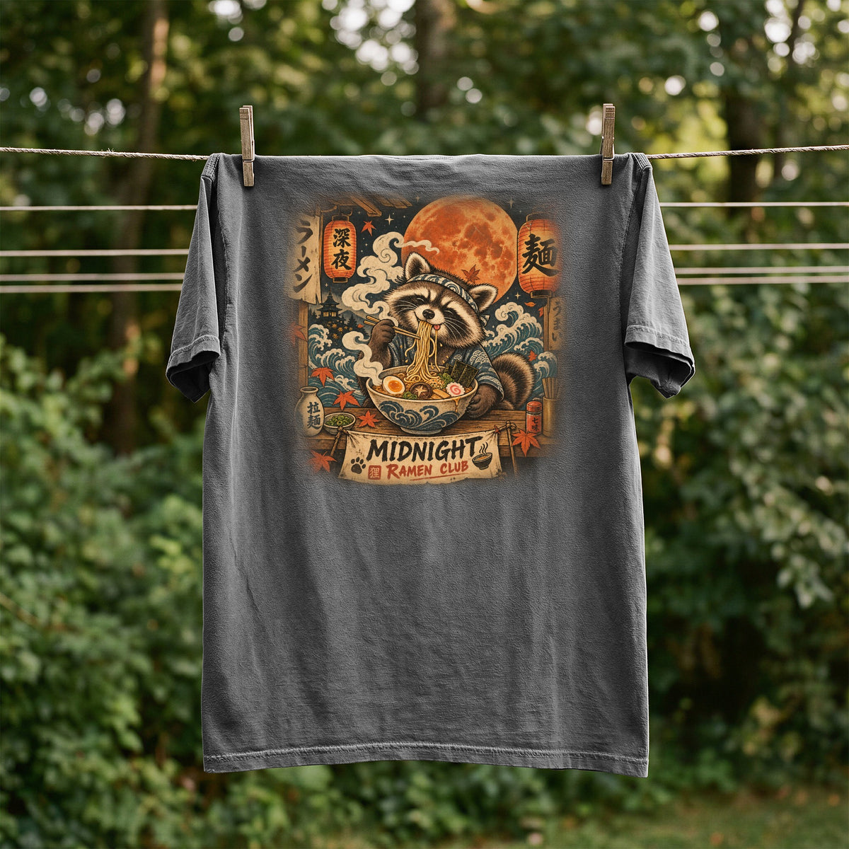Dark grey t-shirt with a raccoon eating ramen under a full moon.