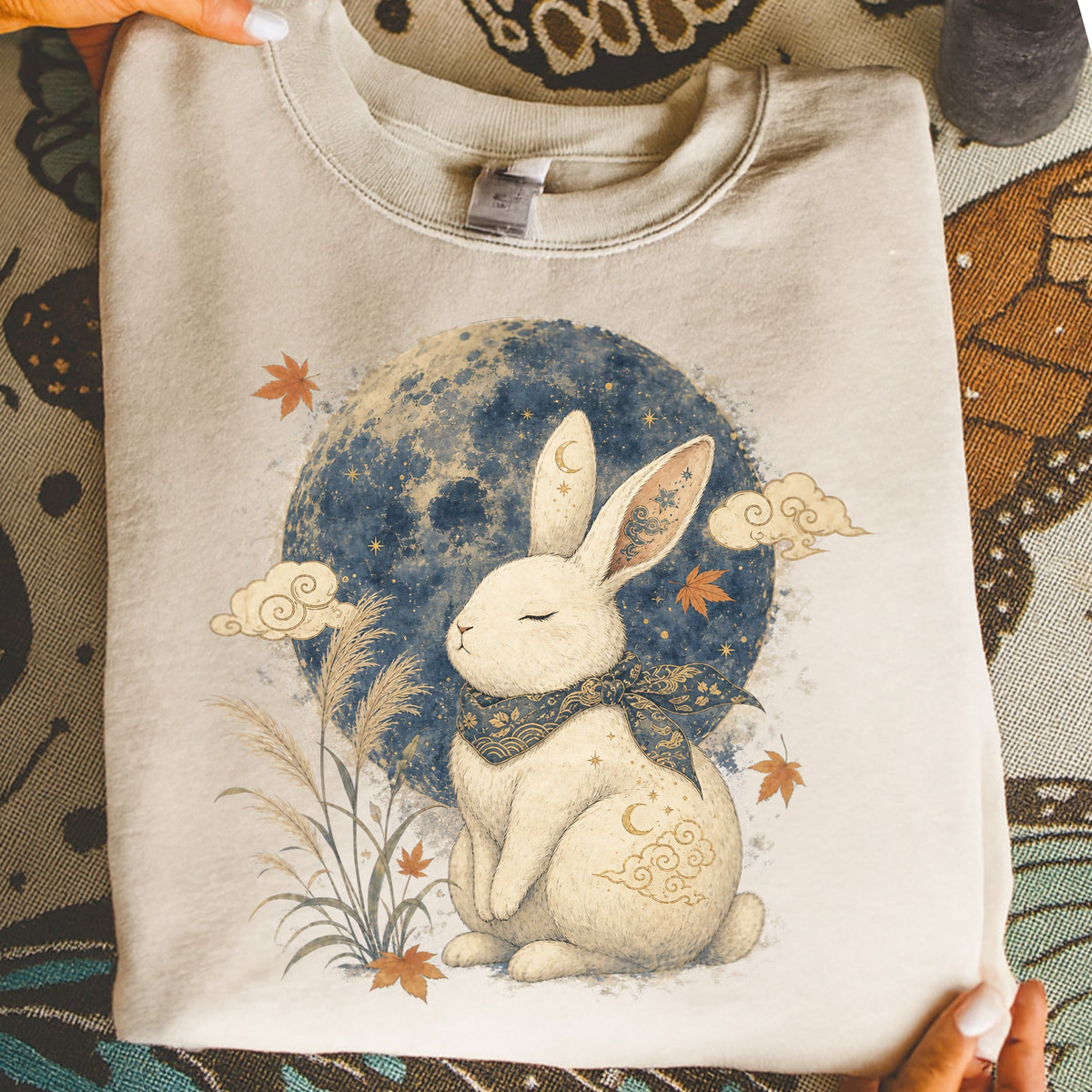 Cream sweatshirt with a white rabbit sitting under a blue, starry moon.