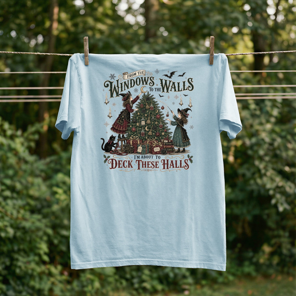 Light blue t-shirt with witches decorating a Christmas tree with bats and the text "I'm About to Deck These Halls".