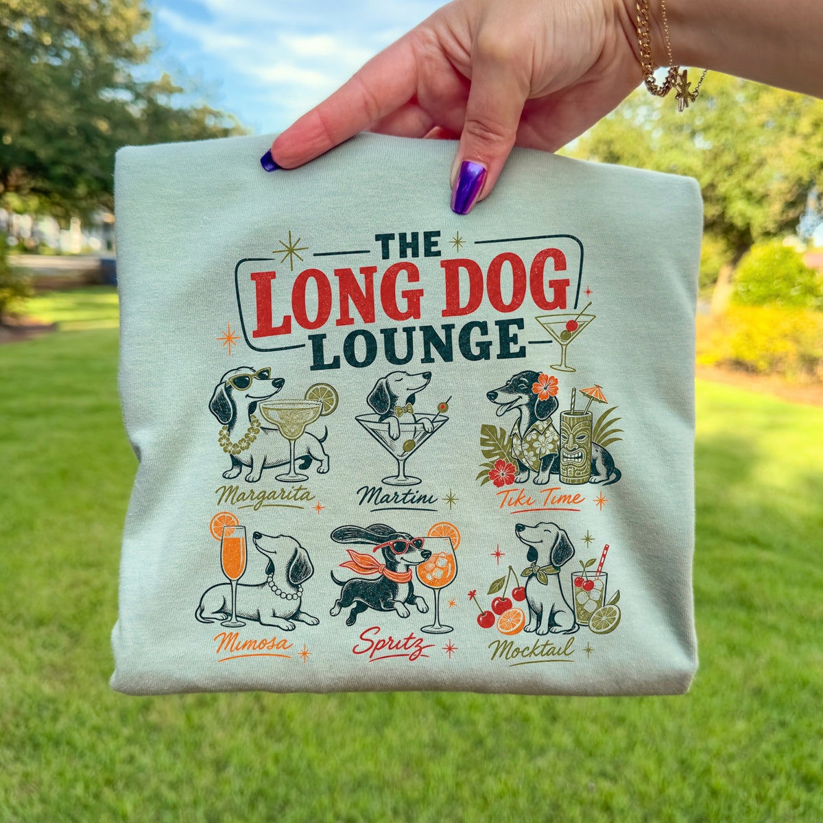 Light green t-shirt with "The Long Dog Lounge" text and six dachshund illustrations with drinks.