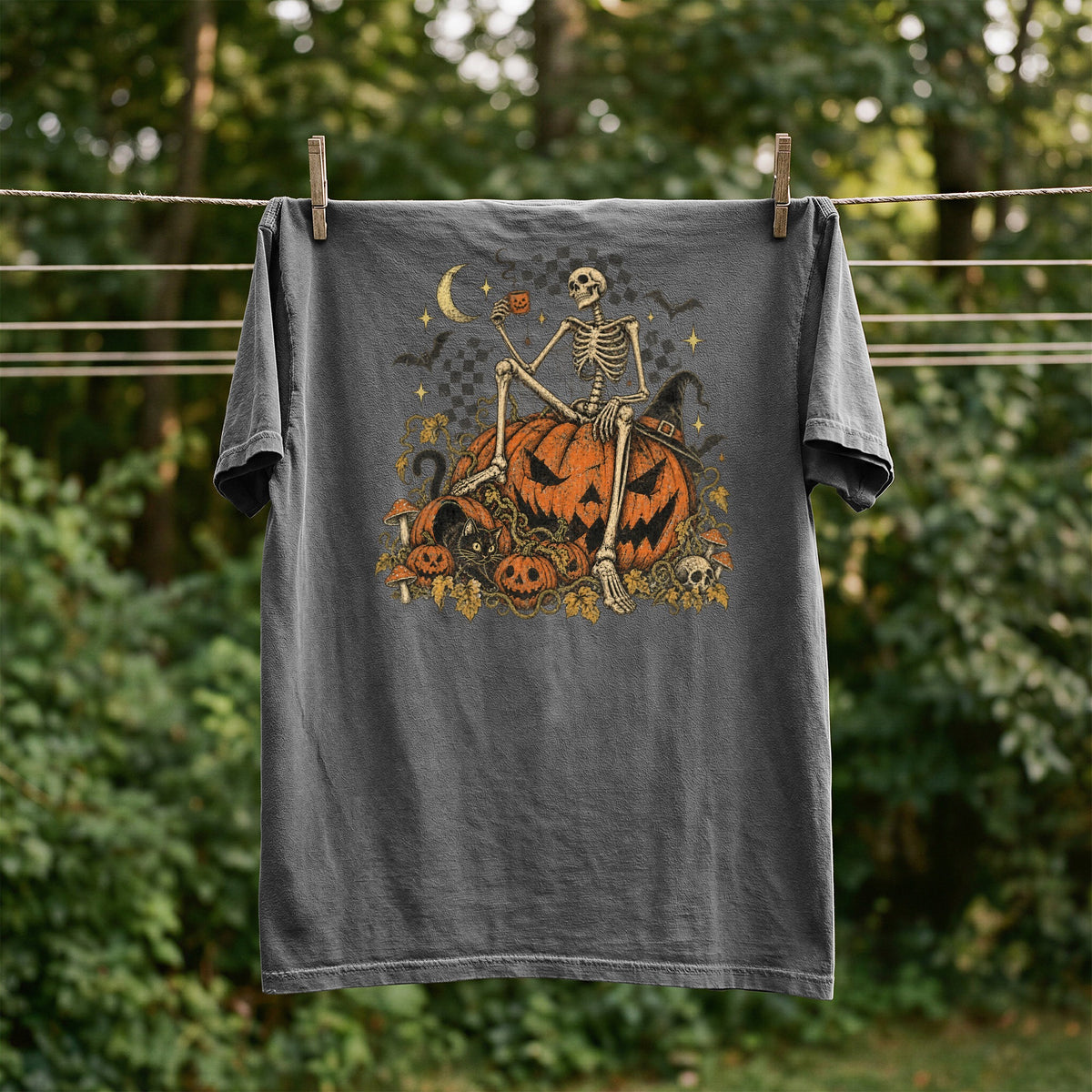 T-shirt with skeleton sitting on pumpkins, crescent moon, bats, and witch hat.