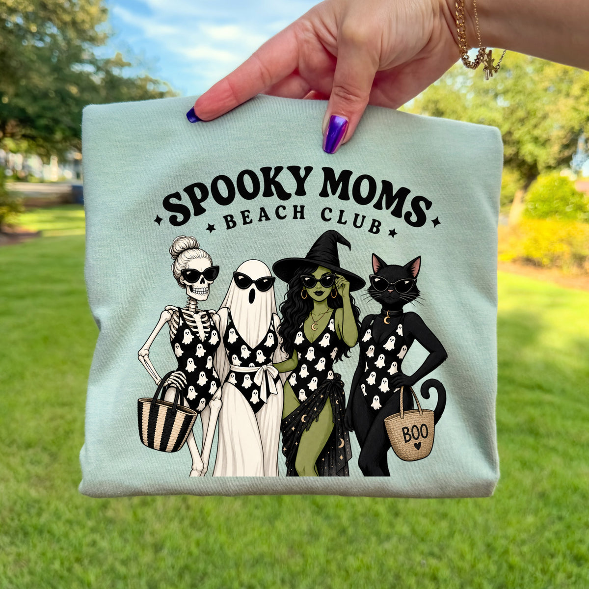 Spooky Moms Beach Club graphic with skeleton, ghost, witch, and black cat on mint green shirt.