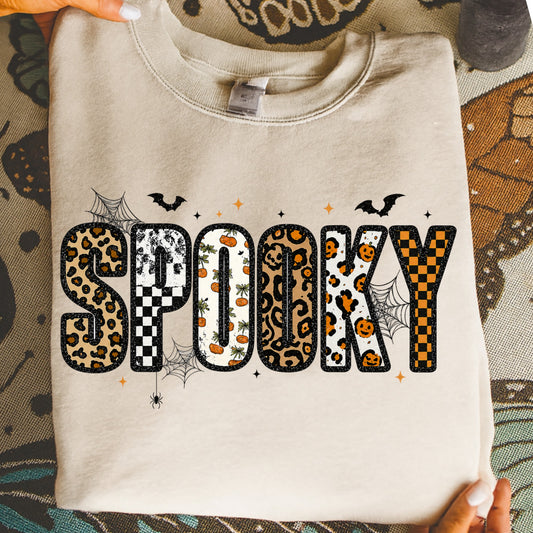 Cream sweatshirt with "SPOOKY" text in leopard, checkerboard, and pumpkin patterns.