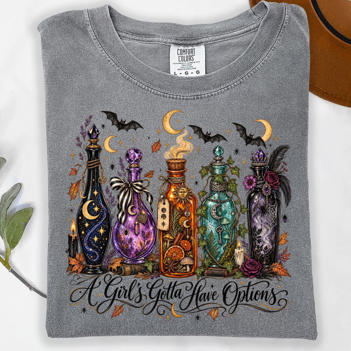Grey t-shirt with graphic of potion bottles, bats, moons, and the text "A Girl's Gotta Have Options".