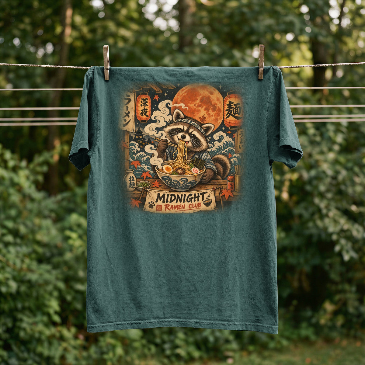 T-shirt graphic of a raccoon eating ramen under a large moon with "Midnight Ramen Club" text.