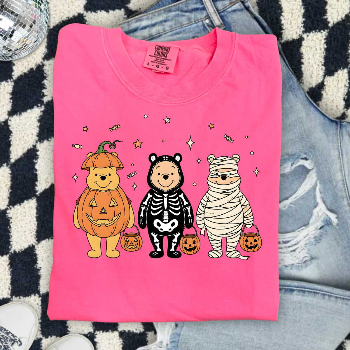 Winnie the Pooh characters dressed as a pumpkin, skeleton, and mummy on a pink shirt.