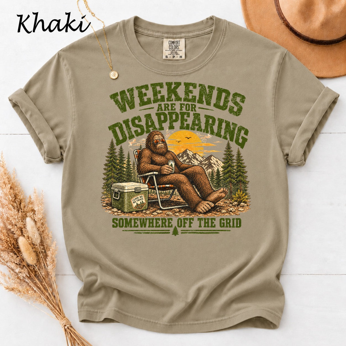 Khaki t-shirt with graphic of Bigfoot sitting in a chair with a drink and cooler.