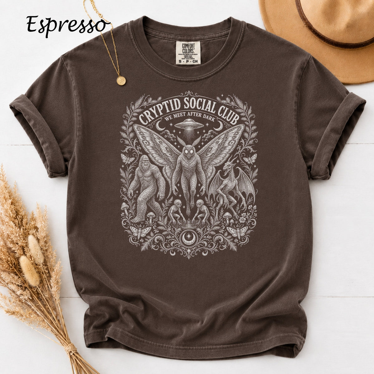 Brown t-shirt with white Cryptid Social Club graphic featuring Bigfoot, mothman, and dragon.