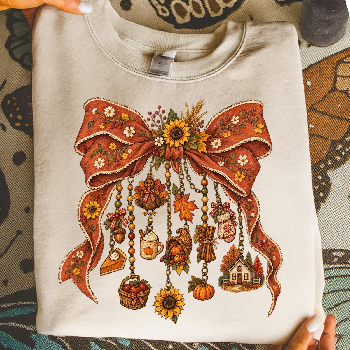 Cream sweatshirt with a rustic fall-themed graphic featuring a bow with hanging charms.