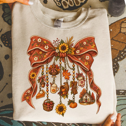 Cream sweatshirt with a rustic fall-themed graphic featuring a bow with hanging charms.