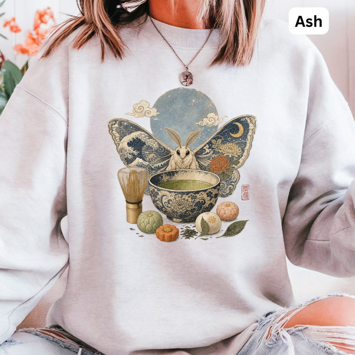 Moth with ornate wings and matcha tea set on a light ash-colored sweatshirt.