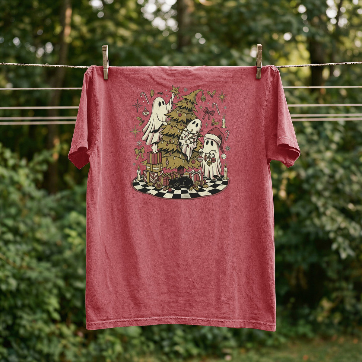 Red t-shirt with ghosts and Christmas tree graphic, hanging on a clothesline.