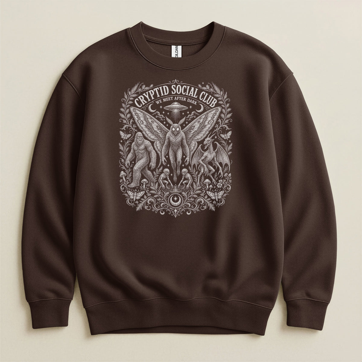 Brown sweatshirt with "Cryptid Social Club We Meet After Dark" graphic featuring creatures.