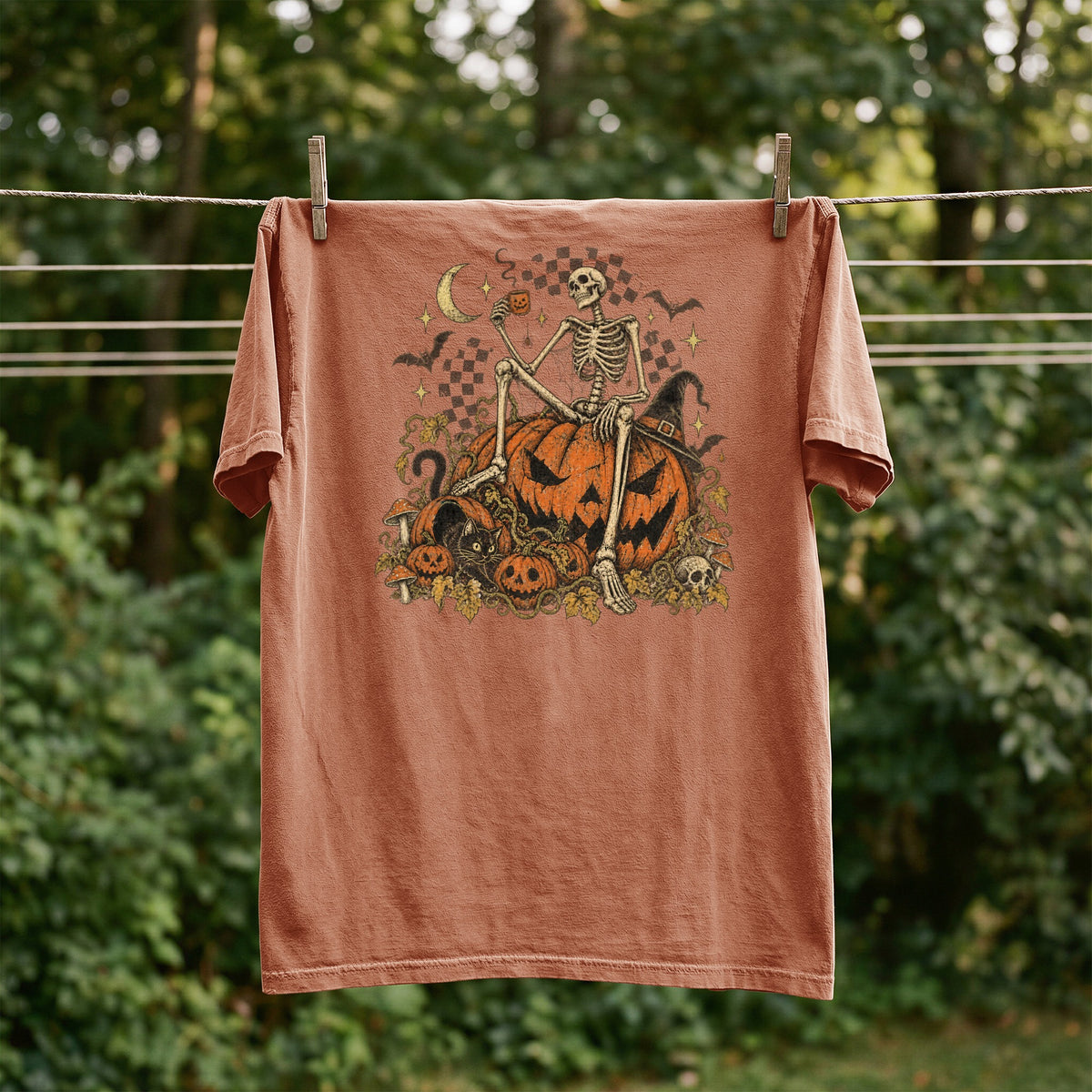 T-shirt with skeleton on pumpkins graphic, Halloween theme, outdoor drying.