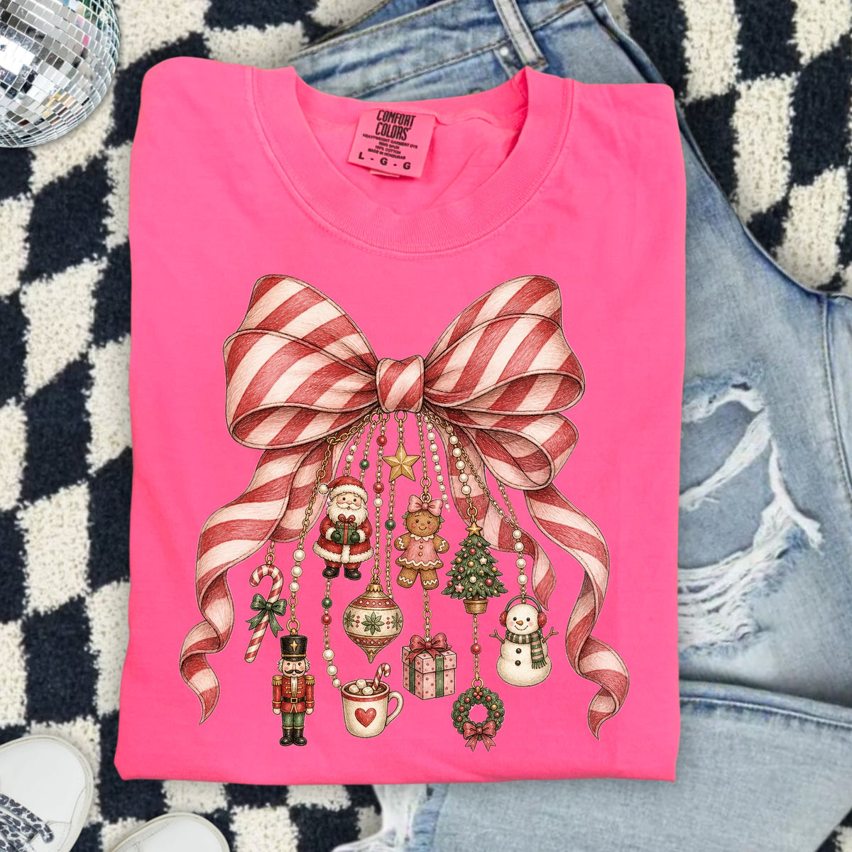 Pink t-shirt with a peppermint bow and various hanging Christmas ornaments.