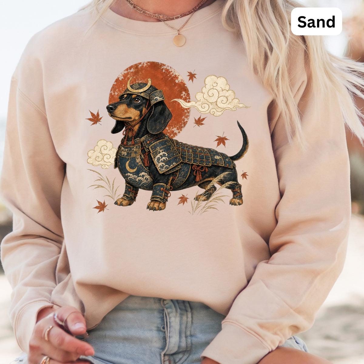 Dachshund wearing samurai armor with moon and clouds graphic on sand-colored sweatshirt.