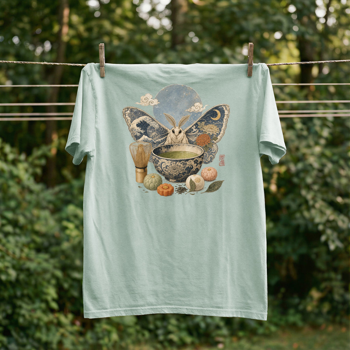 Light green t-shirt with a moth, moon, clouds, matcha bowl, and pastries design.