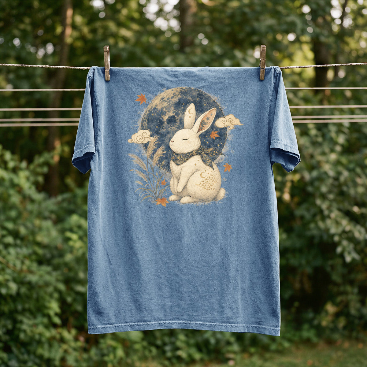 Blue t-shirt with graphic of a white rabbit under a moon, with clouds and leaves.