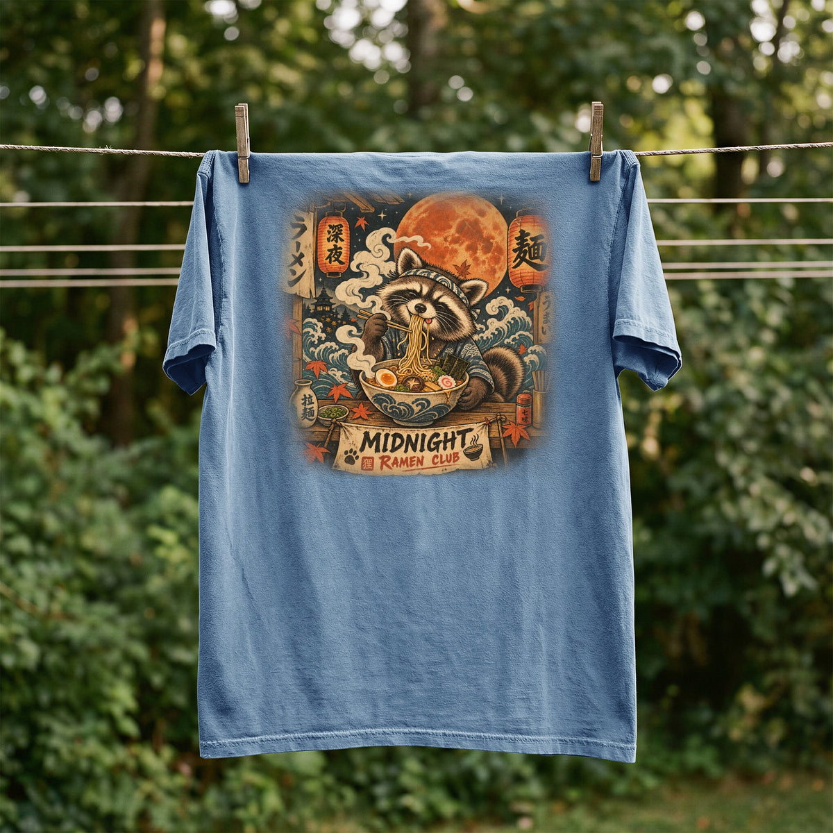 Blue t-shirt with graphic of raccoon eating ramen under a full moon and text "MIDNIGHT RAMEN CLUB".