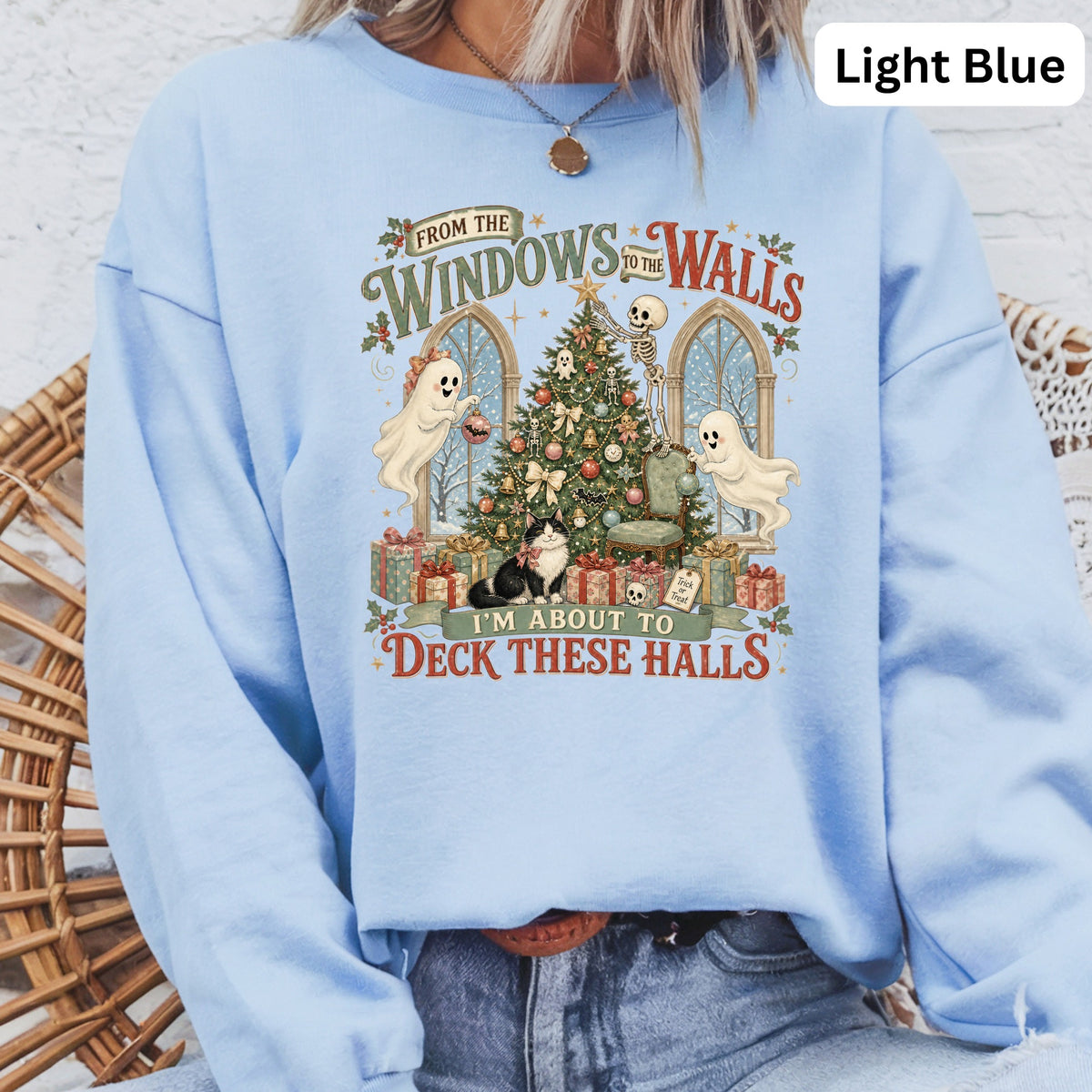 Light blue sweatshirt with Christmas graphic featuring ghosts, skeleton, cat, and tree.