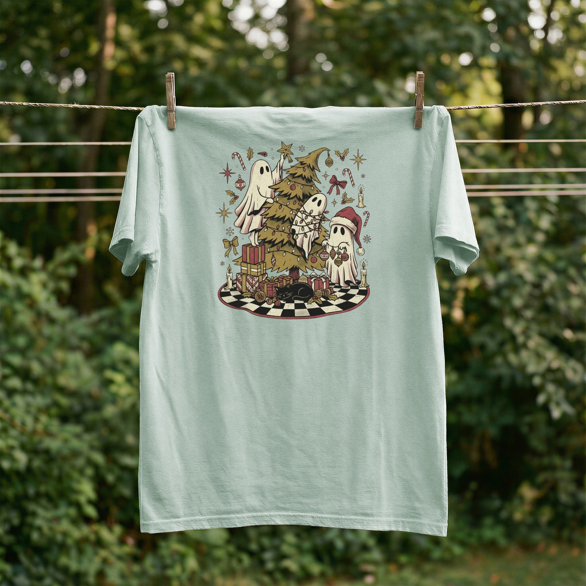 Light green t-shirt with ghosts decorating a Christmas tree on a checkered mat.