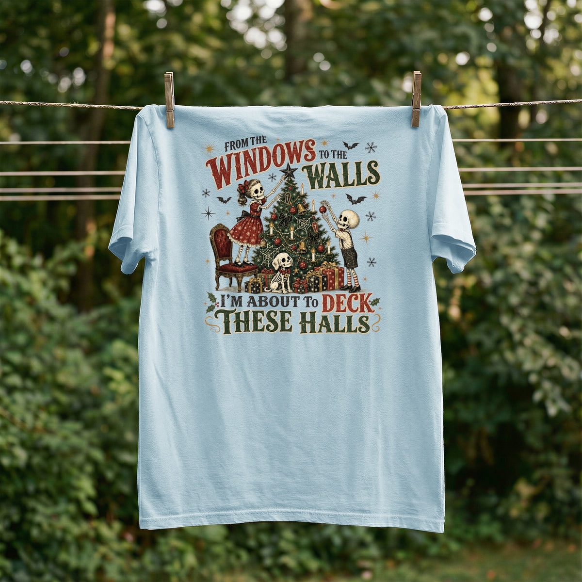 Light blue t-shirt with skeletons decorating a Christmas tree and text.