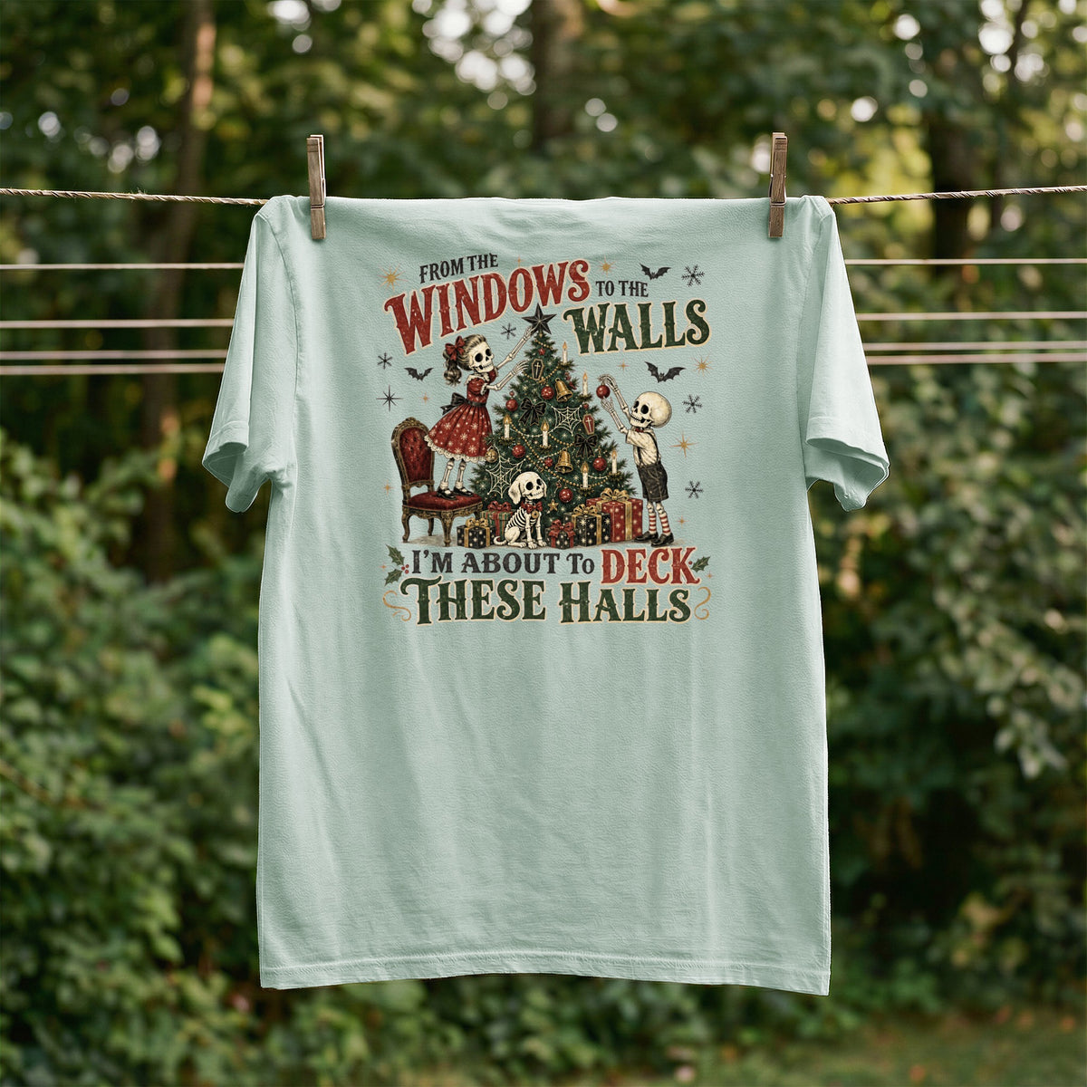 Light green t-shirt with skeleton figures decorating a Christmas tree, text reads "From the Windows to the Walls I'm About to Deck These Halls".