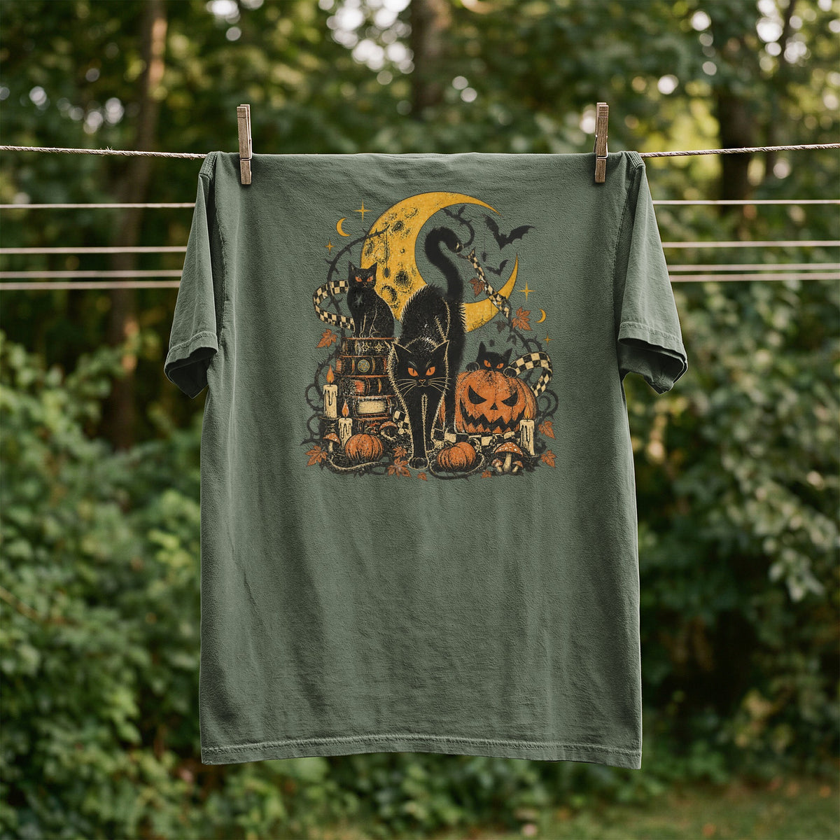 Green t-shirt with Halloween graphic of cats, moon, pumpkins, and books.