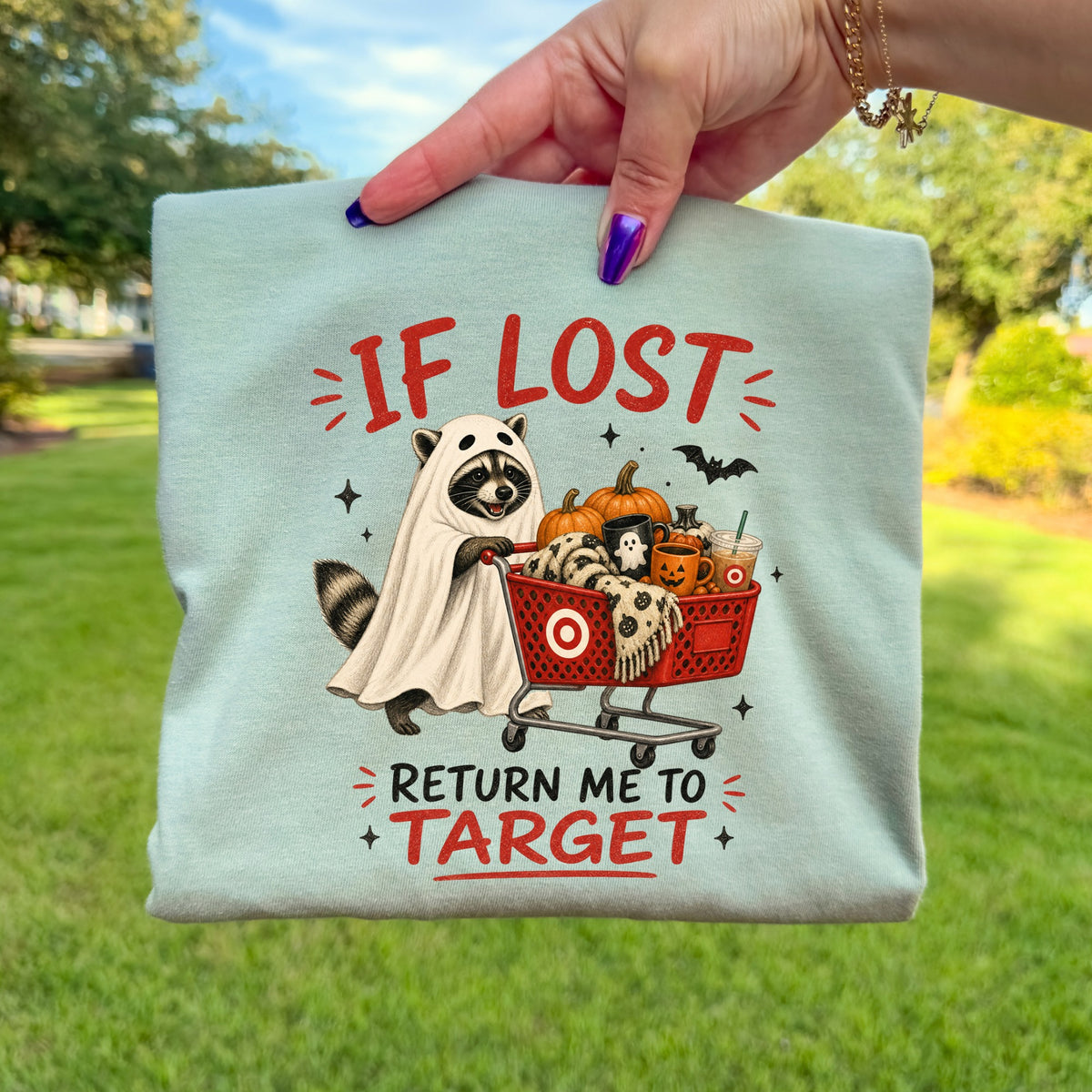 Raccoon in ghost costume pushes shopping cart filled with Halloween items, text "If Lost Return Me To Target".