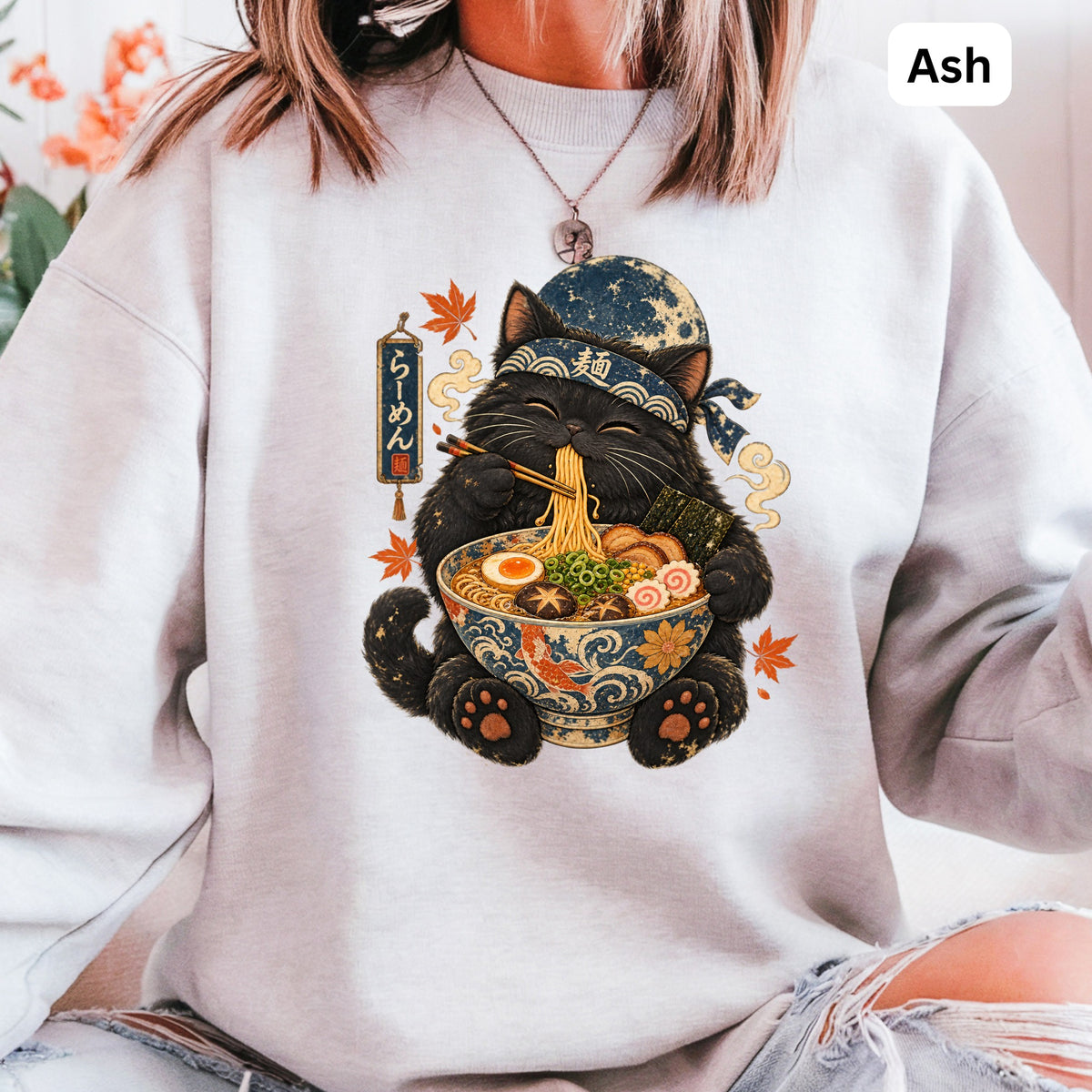 Black cat wearing headband eats ramen from decorative bowl under moon and Japanese text.