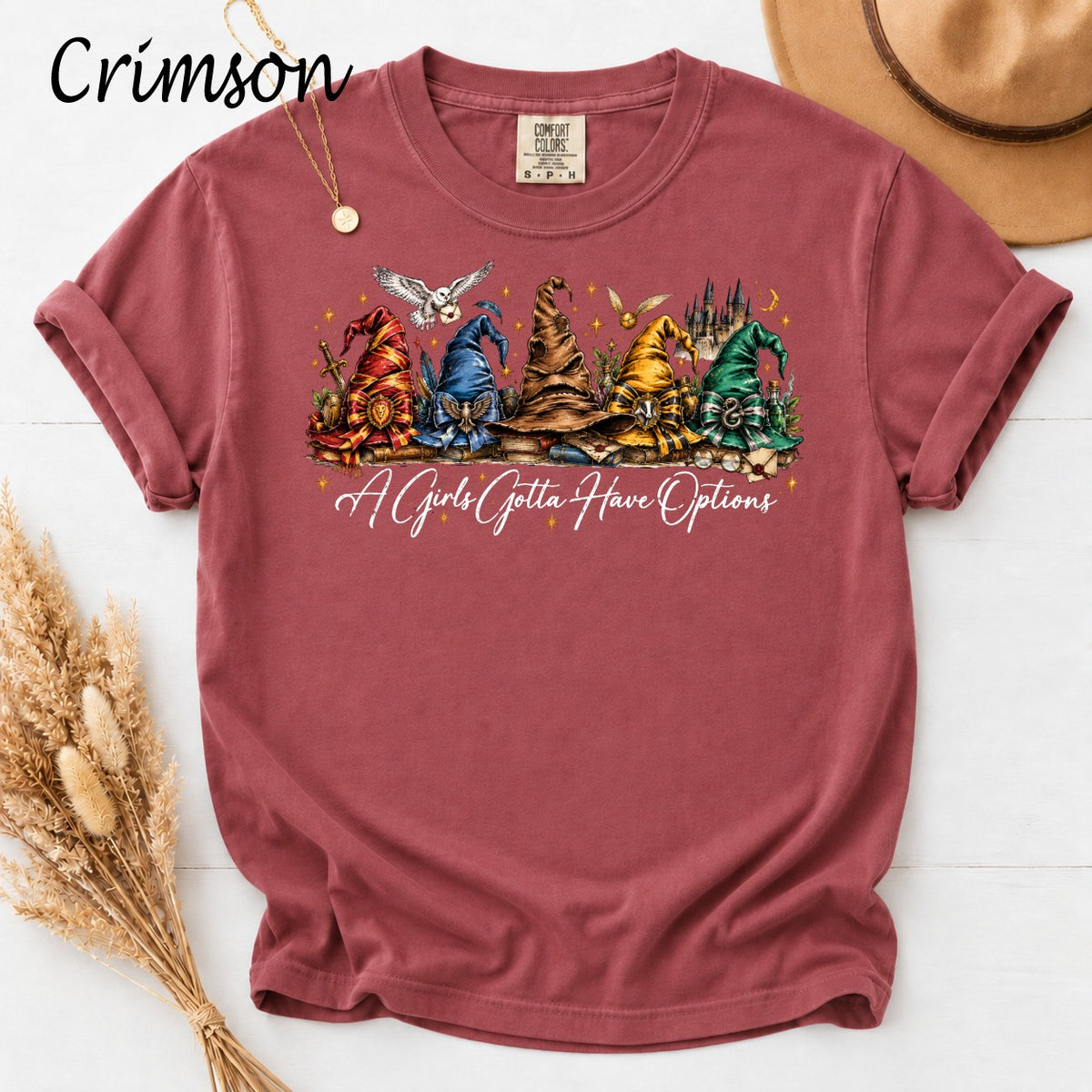 Crimson t-shirt with graphic of five wizard hats and "A Girls Gotta Have Options" text.