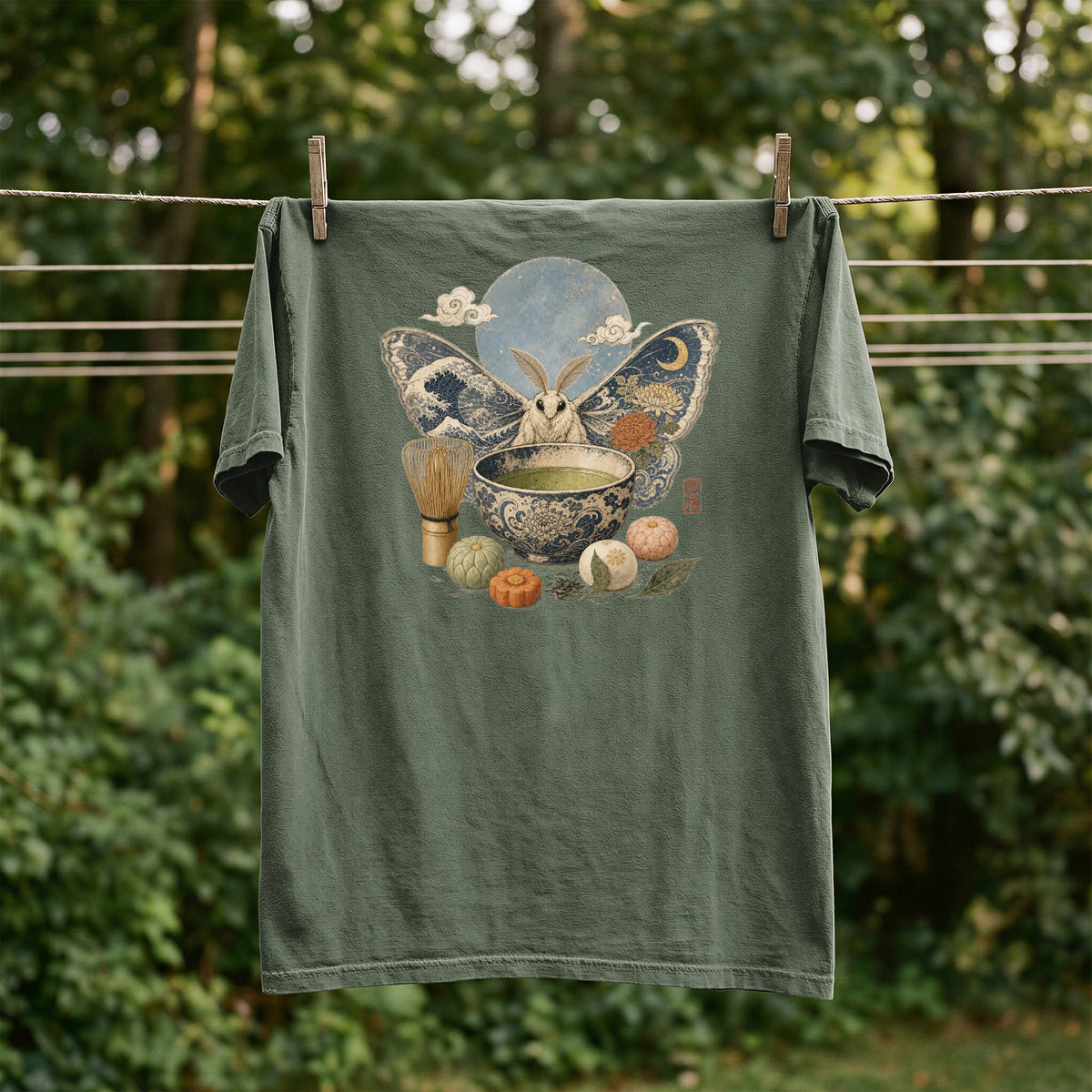 Green t-shirt with a moth, moon, tea bowl, and pastries graphic.