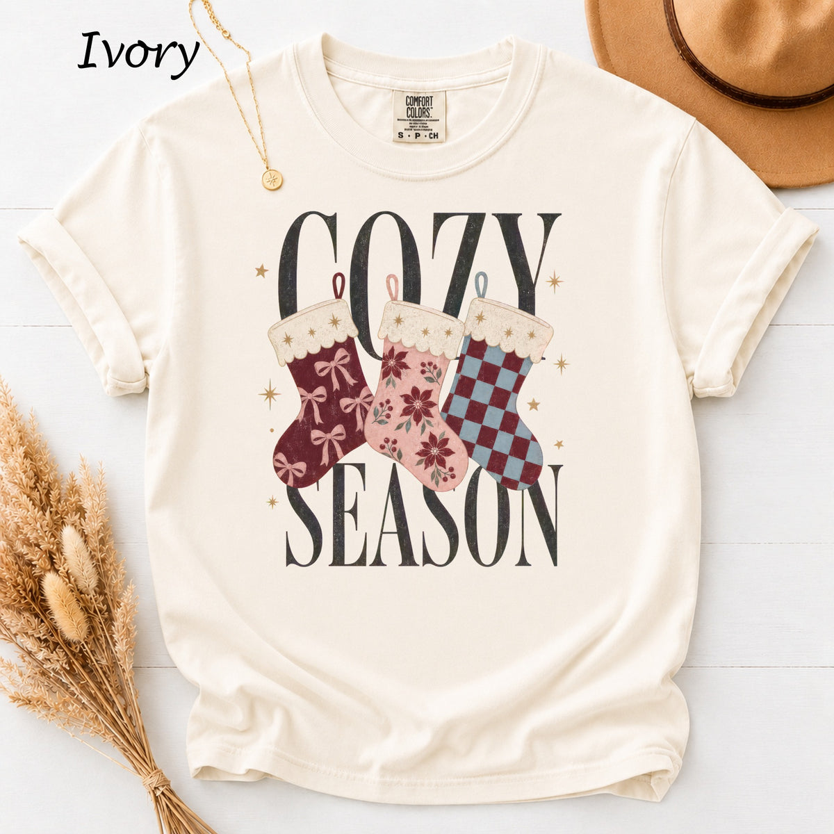 Ivory t-shirt with "Cozy Season" text and three patterned Christmas stockings.