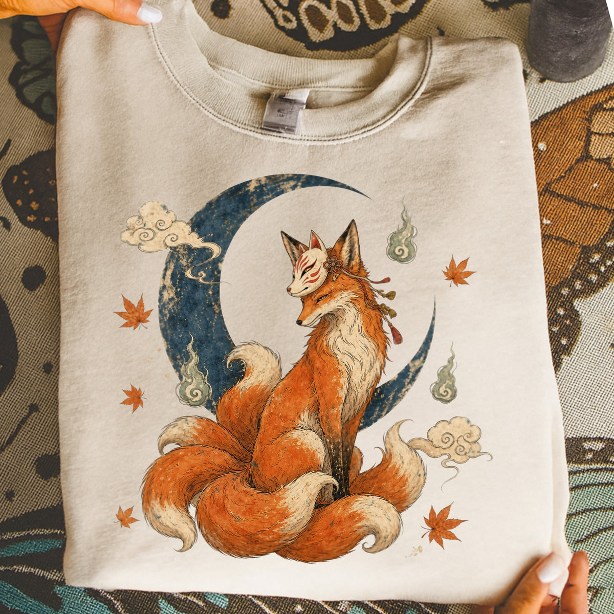 Cream sweatshirt featuring a nine-tailed fox with a mask sitting before a moon.