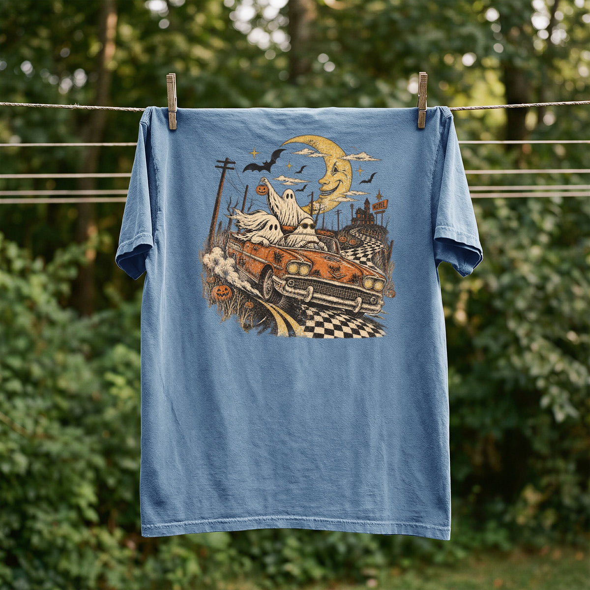 Blue t-shirt with a Halloween graphic of ghosts driving a car past a motel.