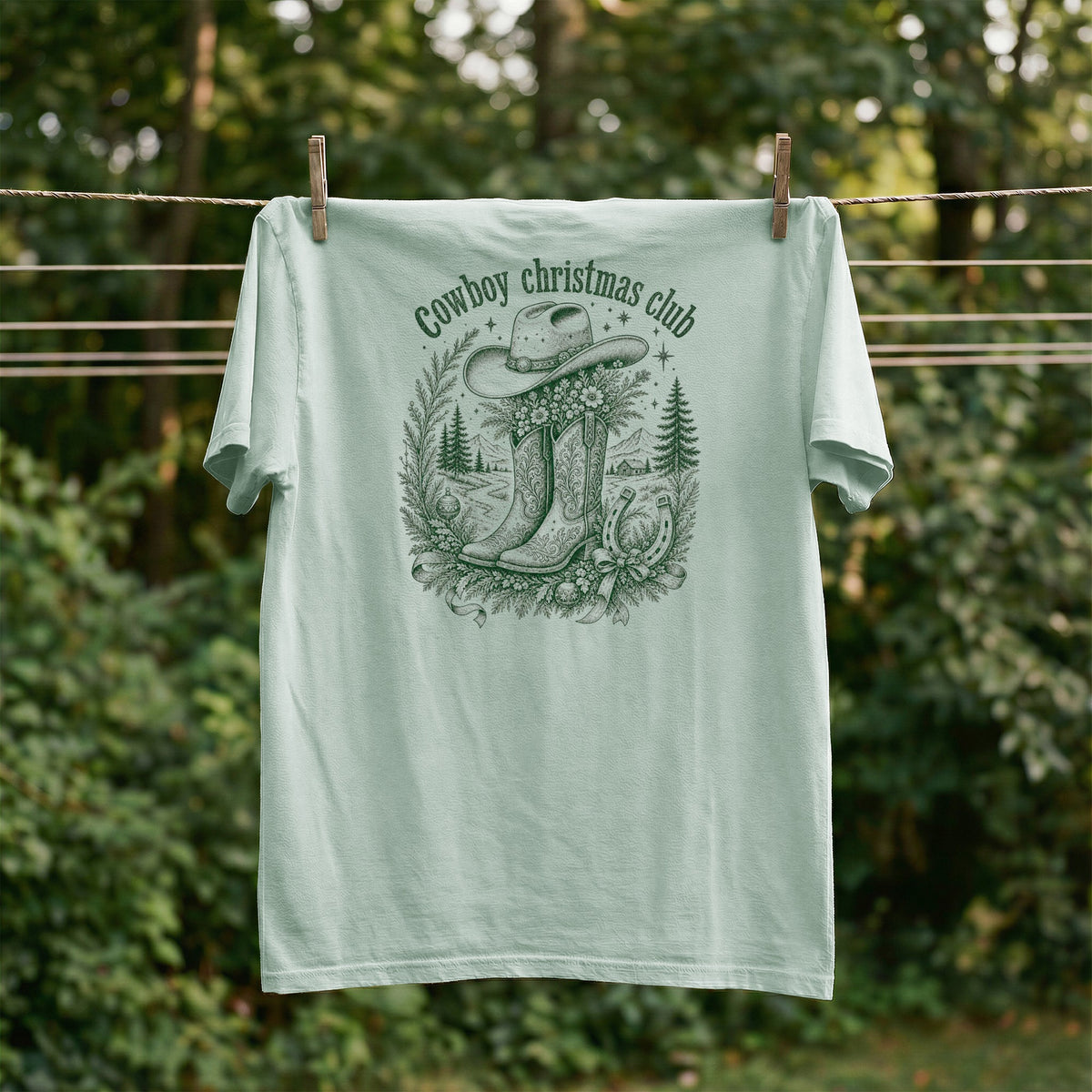 Green t-shirt with "Cowboy Christmas Club" text and a cowboy hat, boots, horseshoe, and pine trees design.